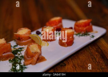 Appetitliche Fischbrötchen aus rotem Fisch mit Füllung im Inneren auf einem weißen Teller und einem Holztisch in einem Restaurant. Leckeres Fischessen Stockfoto