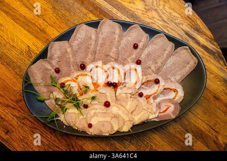 Fleischschnitte auf einem weißen schwarzen Teller auf einem Holztisch. Blick von oben Stockfoto