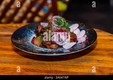 Gegrilltes Fleisch mit gebackenem Gemüse auf einem Teller auf einem Holztisch in einem Restaurant. Leckeres, appetitliches Essen Stockfoto