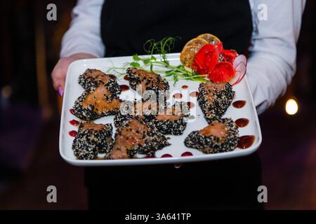 Gegrilltes rotes Fischfleisch mit Sesamsamen in den Händen des Kellners. Teller mit Fisch und Ingwer. Nahaufnahme Stockfoto