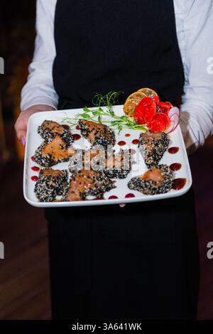 Gegrilltes rotes Fischfleisch mit Sesamsamen in den Händen des Kellners. Teller mit Fisch und Ingwer Stockfoto