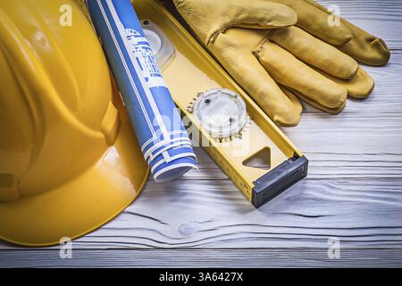 Zusammensetzung der Sicherheitshandschuhe Bauhelm blau gerollte Blaupausen Bauhöhe auf Holzbrett Stockfoto