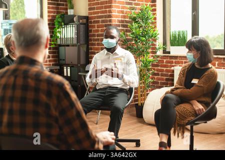 Ein junger schwarzer Mann saß in einem Büro mit Ziegelmauern und teilte seinen Prozess der Depression während der Gruppentherapie mit. afroamerikaner sitzt im Kreis und spricht mit der aa-Gemeinschaft über psychische Gesundheit. Stockfoto