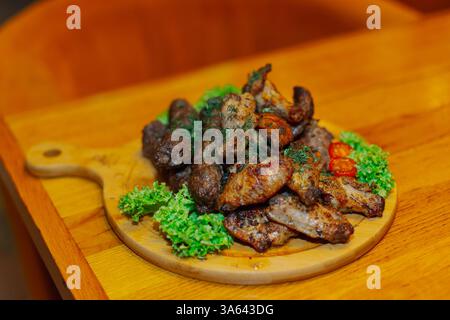 Gebratene Flügel, gebratene Würstchen und gegrilltes Fleisch auf einem Holztablett mit Gemüse Stockfoto