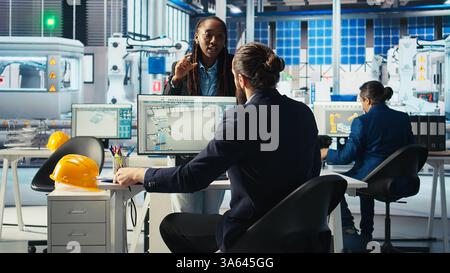 Produktionsleiter der Photovoltaik-Fabrik, der sich die Schaltpläne ansieht und den Arbeiter über die vorzunehmenden Einstellungen anweist. Der Ingenieur von Solarpaneelen sieht sich die Baupläne der Montagelinien an und spricht mit dem Mitarbeiter Stockfoto