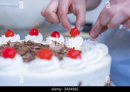 Kuchen ist mit roten Kirschen und Schokolade von Hand dekoriert, Kuchenbacken, Haselstaller Hof Cafe Kuh, Wildberg, Schwarzwald, Deutschland, Europa Stockfoto