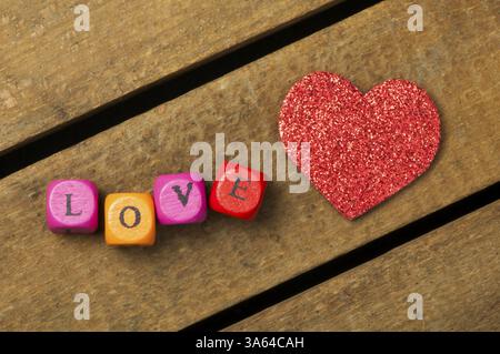 Wortliebe auf bunten Holzwürfeln auf hölzernem Hintergrund und Herz Stockfoto