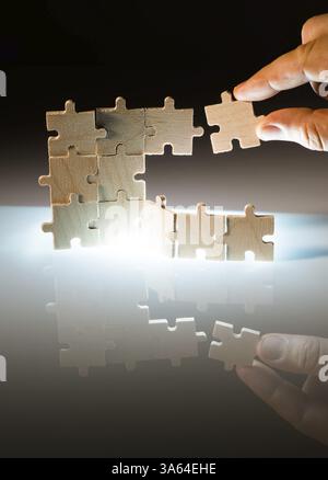 Holzpuzzle und Hintergrund mit Hintergrundbeleuchtung. Vertikal gestapelte Teile. Puzzleteil mit der Hand halten Stockfoto