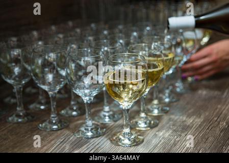 Eine Nahaufnahme des Weißweins, der in Gläser auf einem rustikalen Holztisch gegossen wird, für eine formelle Veranstaltung oder Weinprobe. Stockfoto