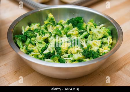 Hellgrüne Brokkoli-Röschen frisch gehackt und in einer Edelstahlschale auf einer Holzarbeitsfläche platziert, fertig zum Kochen oder Servieren. Stockfoto