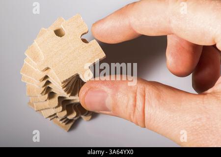 Holzpuzzle auf weißem Hintergrund. Puzzle-Stapel. Puzzleteil mit der Hand halten Stockfoto