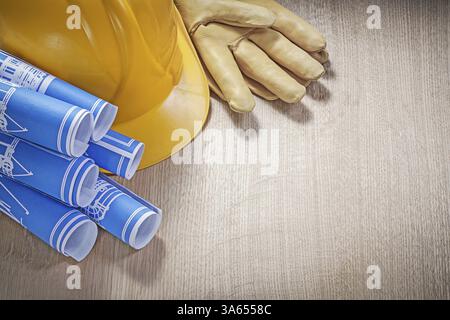 Blau gerollte Konstruktionszeichnungen Schutzhandschuhe aus Leder mit Schutzhelm auf Holzbrett Stockfoto
