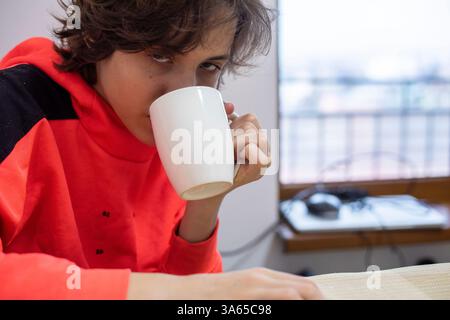 Teenager trinkt heiße Schokolade mit Himbeeren aus einer weißen großen Tasse am Tisch Stockfoto