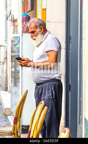 Arabischer Restaurantarbeiter, der in der Tür steht und das Smartphone überprüft - Tours, Indre-et-Loire (37), Frankreich. Stockfoto
