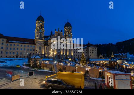 Das Benediktinerabtei Einsiedeln mit seiner mächtigen Basilika in der blauen Stunde und dem Weihnachtsmarkt auf dem Vorderplatz. Stockfoto