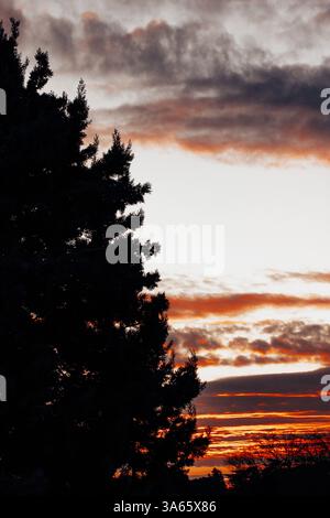 Herrlicher roter, grauer Sonnenuntergang mit dunklen, niedrigen Wolken am Horizont am Ende eines Tages. Majestätische abendliche Landschaft. Bewölkte Landschaft. Vertikales landschaftliches Pgoto. Stockfoto