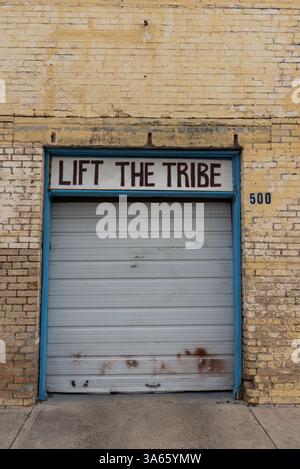 Eine Rollladentür mit den Worten Life the Tribe an der Außenseite eines verlassenen Gebäudes in McAllen, Hidalgo County, Texas, USA. Stockfoto