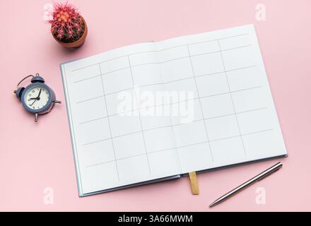 Offenes Notizbuch mit Stift, Wecker und Kakteen auf rosa Hintergrund für Planung und Produktivität Stockfoto