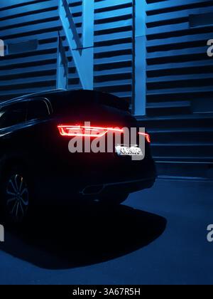 Auto in der Nachtstadt. Heckteil eines schwarzen Renault SUV mit beleuchteten Rückleuchten, blau leuchtende Wand im Hintergrund. Stockfoto