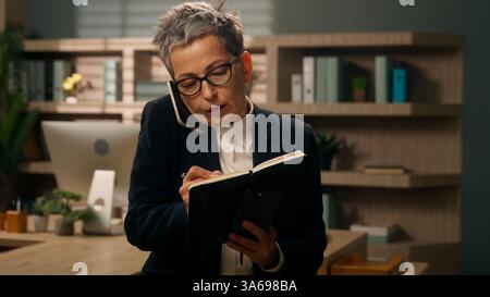 Stress beschäftigt Multitasking Geschäftsfrau Kaukasische Seniorin Geschäftsfrau mittleren Alters Reife Frau arbeitet im Büro telefonisch Notizen schreiben Stockfoto