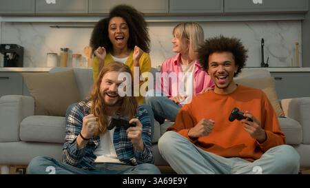 Vier multirassische Leute Freunde Studenten lustiges Wochenende zu Hause kaukasische Männer Männer spielen Konsolen Videospiel süchtig Gewinn verloren Afroamerikaner Stockfoto