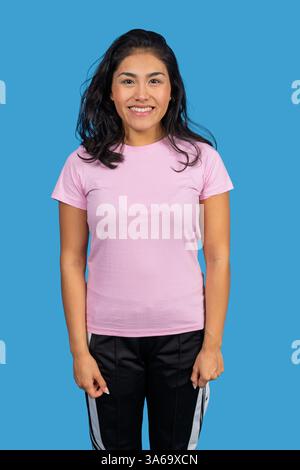 Studio-Porträt einer fröhlichen jungen lateinfrau in lässiger Kleidung, die vor einem leuchtend blauen Hintergrund selbstbewusst lächelt Stockfoto