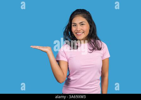 Junge lateinfrau, die etwas auf blauem Hintergrund zeigt und präsentiert Stockfoto