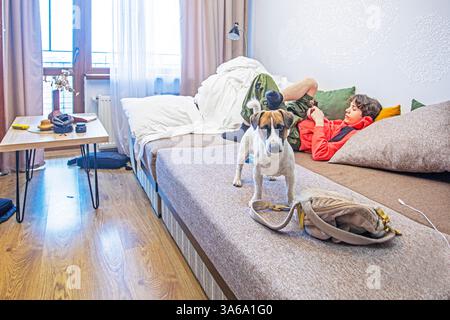 Junge spielt ein Spiel neben Jack russell Terrier auf dem Sofa im Zimmer Stockfoto