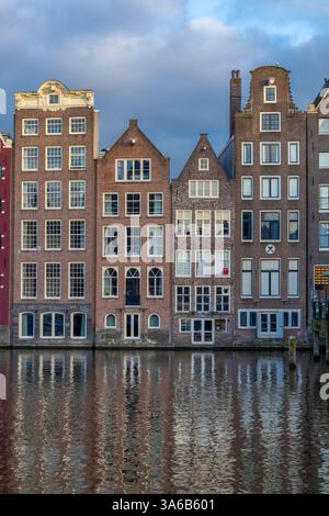 Reihen von Häusern in Amsterdam, krumm und tanzend entlang des Kanals, mit dem Wasser. Stockfoto