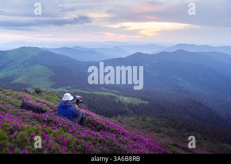 Ein Fotograf bei der Arbeit in einer atemberaubenden Sommerberglandschaft mit blühenden Rhododendron- und Sonnenaufgangstönen Stockfoto