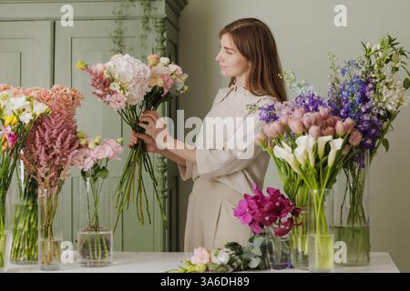Blumenhändler arrangiert elegante Blumenstrauße im Blumenladen, umgeben von frischen Blüten und lächelnd vor Freude. Blumenladen Stockfoto