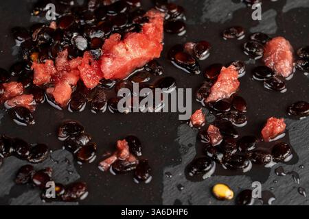 Wassermelonenkerne und rotes Fruchtfleisch auf schwarzem Schiefer, Wassermelonenkerne nach dem Schälen auf schwarzem Stein Stockfoto