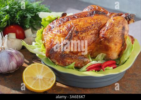 Ein perfekt geröstetes Huhn sitzt auf einem Bett aus knusprigem Salat, umgeben von lebendigem Gemüse und einer Zitrone, bereit für einen Familientreffen. Stockfoto