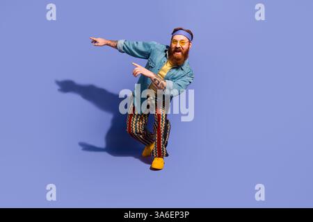 Trendiger bärtiger Mann in lebendigem Outfit vor violettem Hintergrund, der Freude und Positivität ausdrückt und Mode zeigt Stockfoto