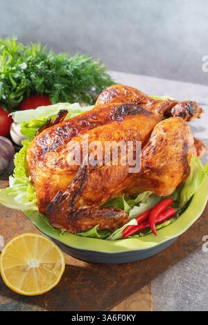 Ein perfekt geröstetes Huhn sitzt auf einem Bett aus knusprigem Salat, umgeben von lebendigem Gemüse und einer Zitrone, bereit für einen Familientreffen. Stockfoto