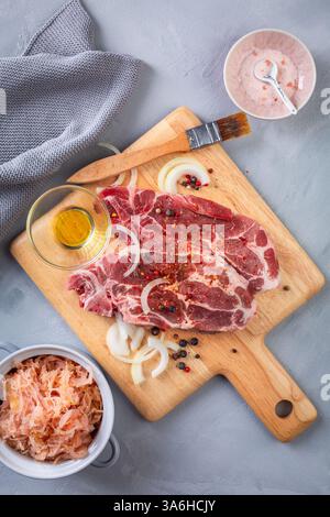 Rohes Schweinefleisch. Frische Steaks auf Schneidebrett mit Salz, Zwiebeln und Sauerkraut Stockfoto