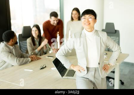 Eine Gruppe verschiedener Fachleute führte in einem sonnendurchfluteten Büro lebhafte Diskussionen. Eine Frau steht selbstbewusst und zeigt Teamarbeit und Zusammenarbeit i Stockfoto