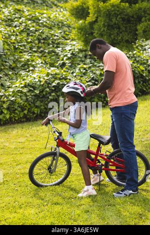 Vater passt den Helm der Tochter an, während sie sich auf das Radfahren im Park vorbereitet Stockfoto