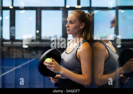 Konzentrierte Frau, die Ballschläger und Ball hält und sich auf das Spiel auf dem Court vorbereitet Stockfoto