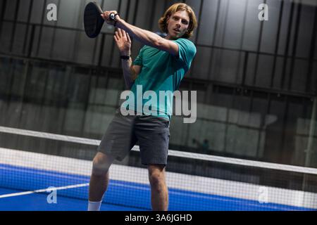 Junger Mann, der Padel-Tennis spielt, Schläger schwingen mit Fokus und Entschlossenheit Stockfoto