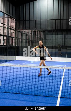 Frau spielt Padel-Tennis auf dem Hallenplatz, fokussiert auf Ball, Kopierraum Stockfoto