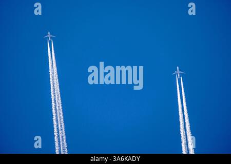 Zwei weiße Jets fliegen parallel und zeichnen lange Kondensstreifen vor einem blauen Himmel als Hintergrund Stockfoto
