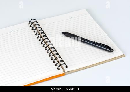 Der Stift und die leere Seite: Ein eleganter schwarzer Stift liegt auf einem frischen, offenen Notizbuch, ein Symbol für Kreativität und den Akt der Dokumentierung von Gedanken auf weißem Blac Stockfoto
