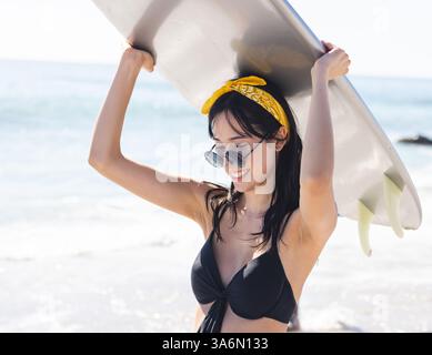 Lächelnde Frau in Sonnenbrille mit Surfbrett am sonnigen Strandtag Stockfoto