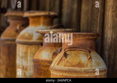Vier rostige, antike Milchkannen aus Metall, die neben einem Holzgebäude stehen. Stockfoto