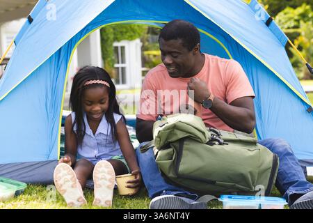 Vater und Tochter genießen Camping und packen den Rucksack zusammen im Gartenzelt aus Stockfoto