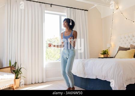 Junge Frau tanzt fröhlich im Schlafzimmer, trägt Kopfhörer und genießt Musik Stockfoto