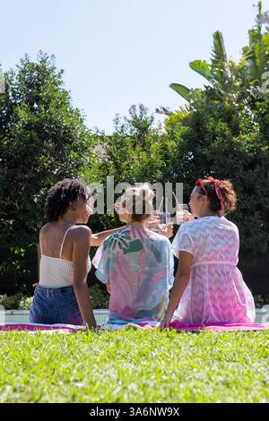 Entspannen Sie am Pool, verschiedene weibliche Freunde teilen Drinks und Sonnenschein und schaffen Sie fröhliche Momente Stockfoto