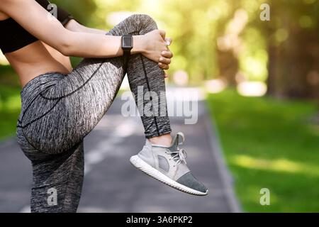 Weibliche Athletin, die sich auf das morgendliche Joggen im Park vorbereitet und die Beinmuskulatur dehnt Stockfoto