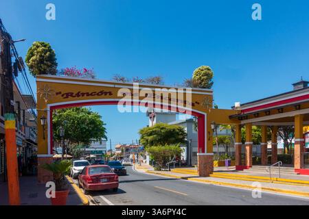 Rincón, PR - USA - 16. März 2025 Ein lebendiger Eingangsbogen in Rincón, Puerto Rico, heißt „Rincón me Encanta“ und heißt Besucher willkommen. Die Straße ist gesäumt von Stockfoto